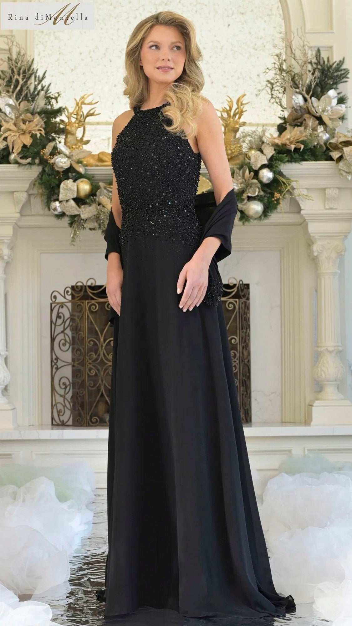 A woman wearing the Rina Di Montella RD3304 long black formal dress stands before a decorated white mantel with gold and green accents.